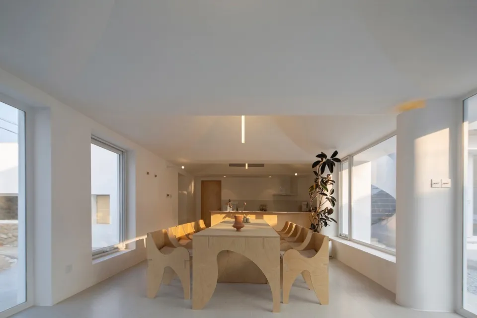 Modern minimalist dining room interior featuring wooden table, chairs, and glass windows, with a potted plant adding life to
