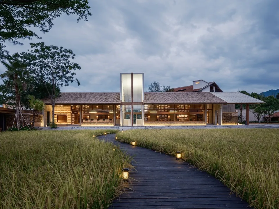 A modern building with wooden exterior and lighting along a pathway surrounded by grass.