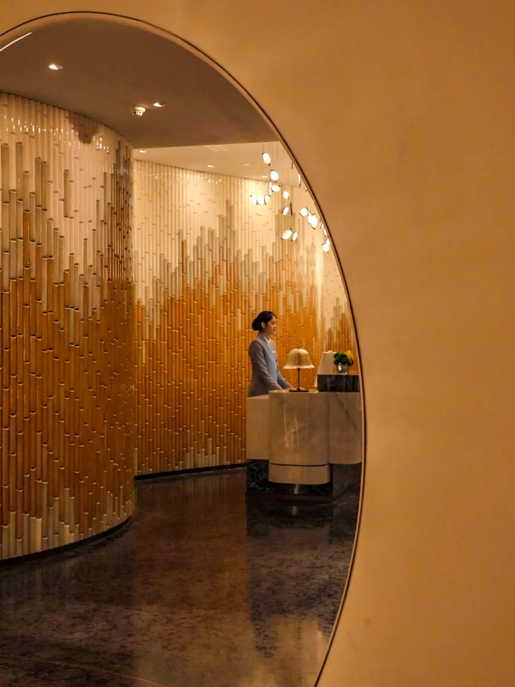 A modern hotel lobby featuring marble tiles, wooden panels, and ambient lighting.
