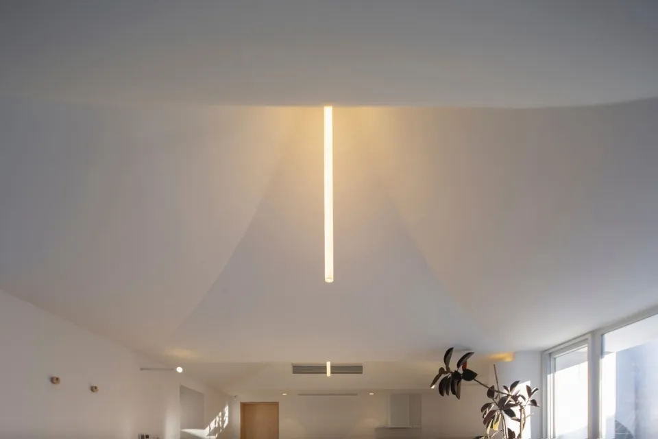 A modern room with a linear light fixture hanging from the ceiling, casting warm, indirect light.
