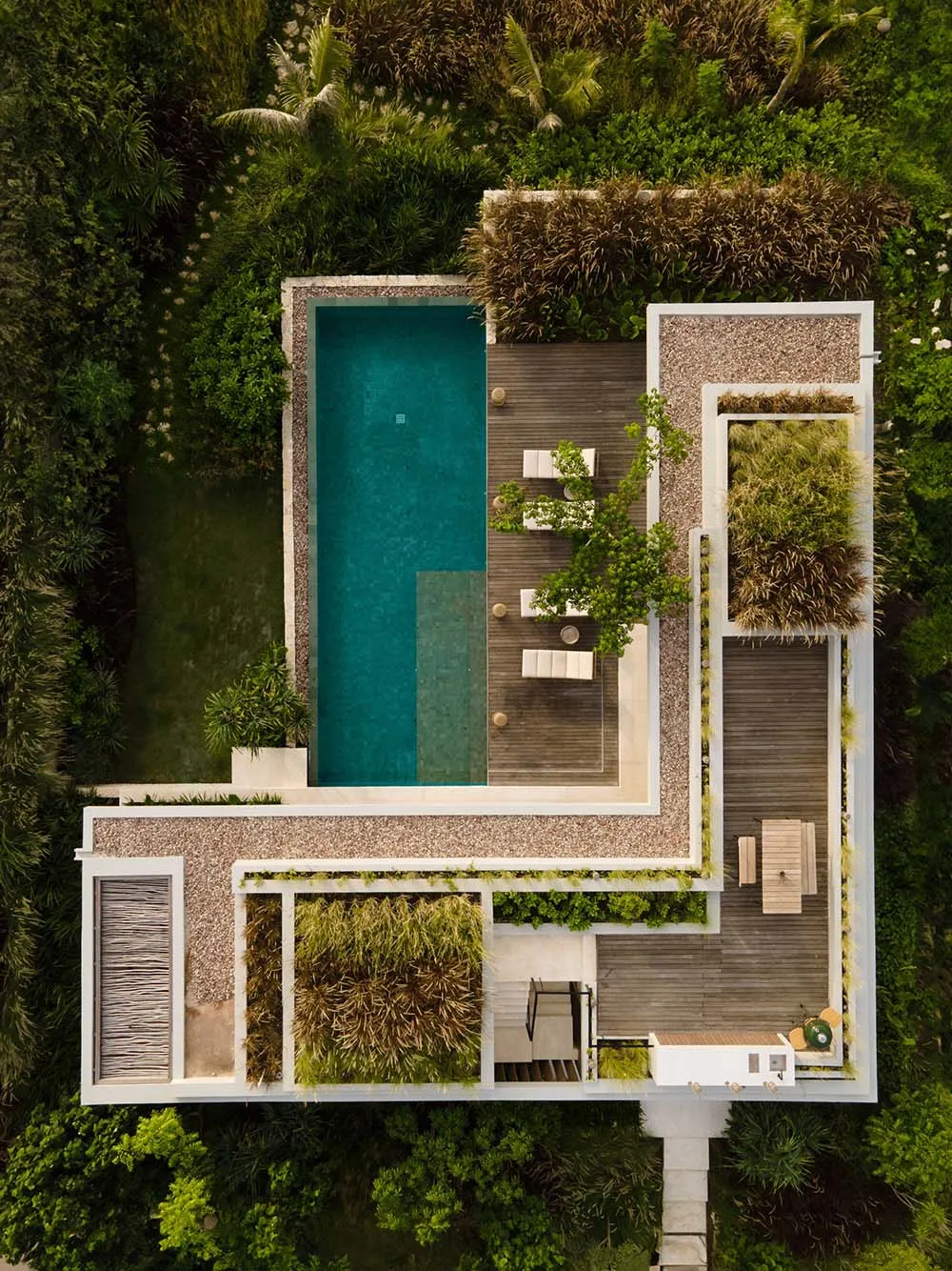 A modern minimalist residential exterior featuring a pool, wooden deck, gravel pathway, and lush greenery.
