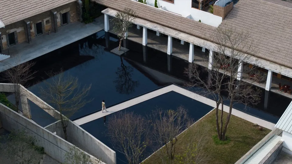 An aerial view of a modern swimming pool with a concrete floor and a clear pool filled with water, surrounded by buildings.