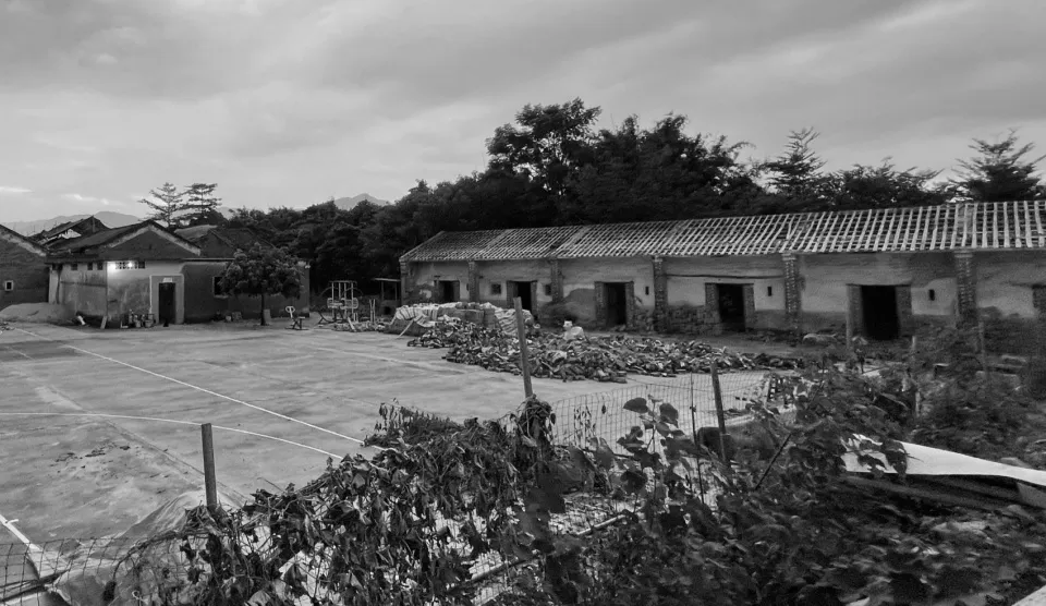 An old, rural building constructed with concrete and gravel, surrounded by trees.