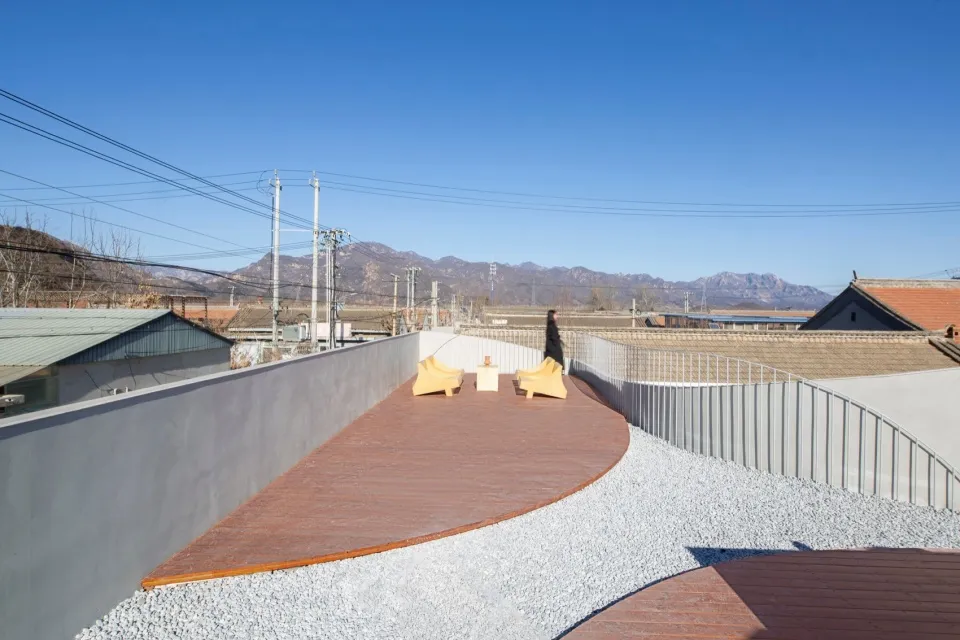 A minimalist roof deck featuring wood planks, with a person walking in the background.