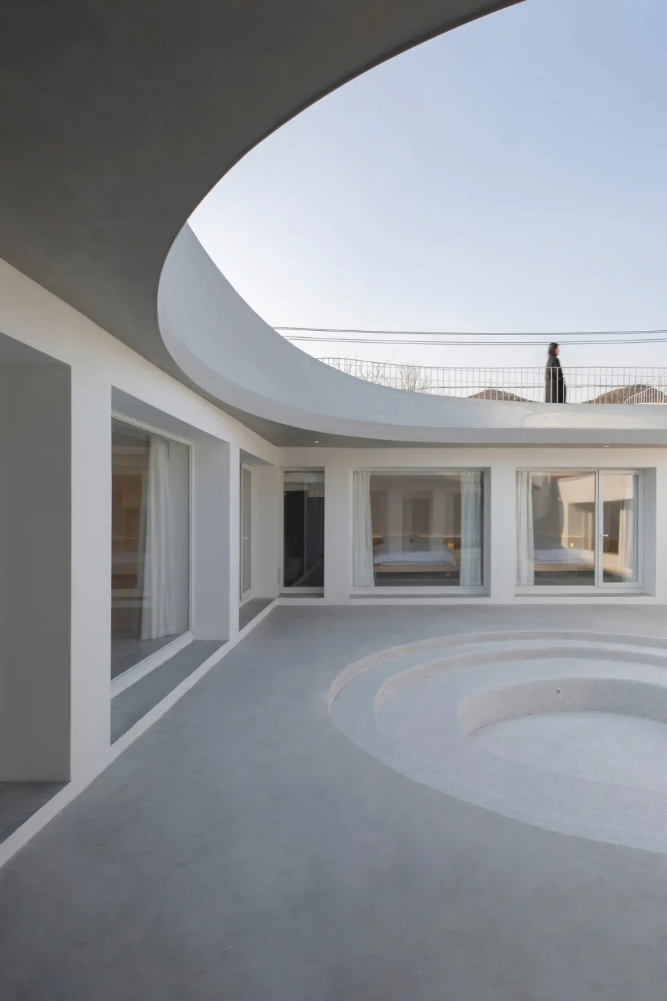 Modern minimalist residential interior featuring a circular concrete floor and large glass windows.