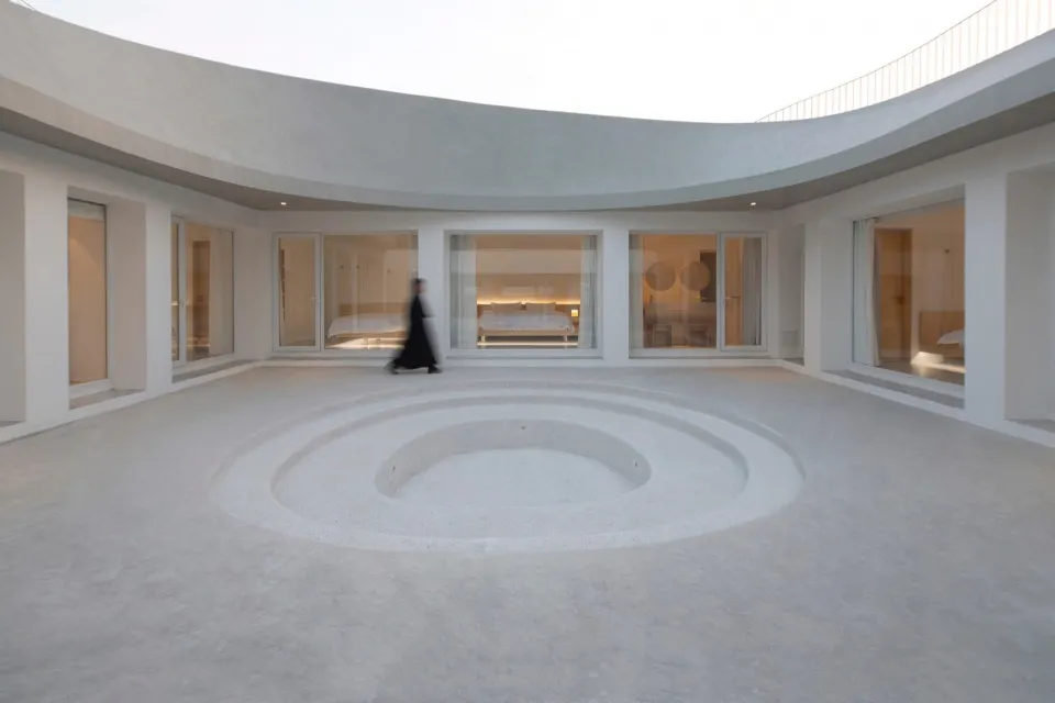Circular minimalist interior space with concrete flooring and large windows.