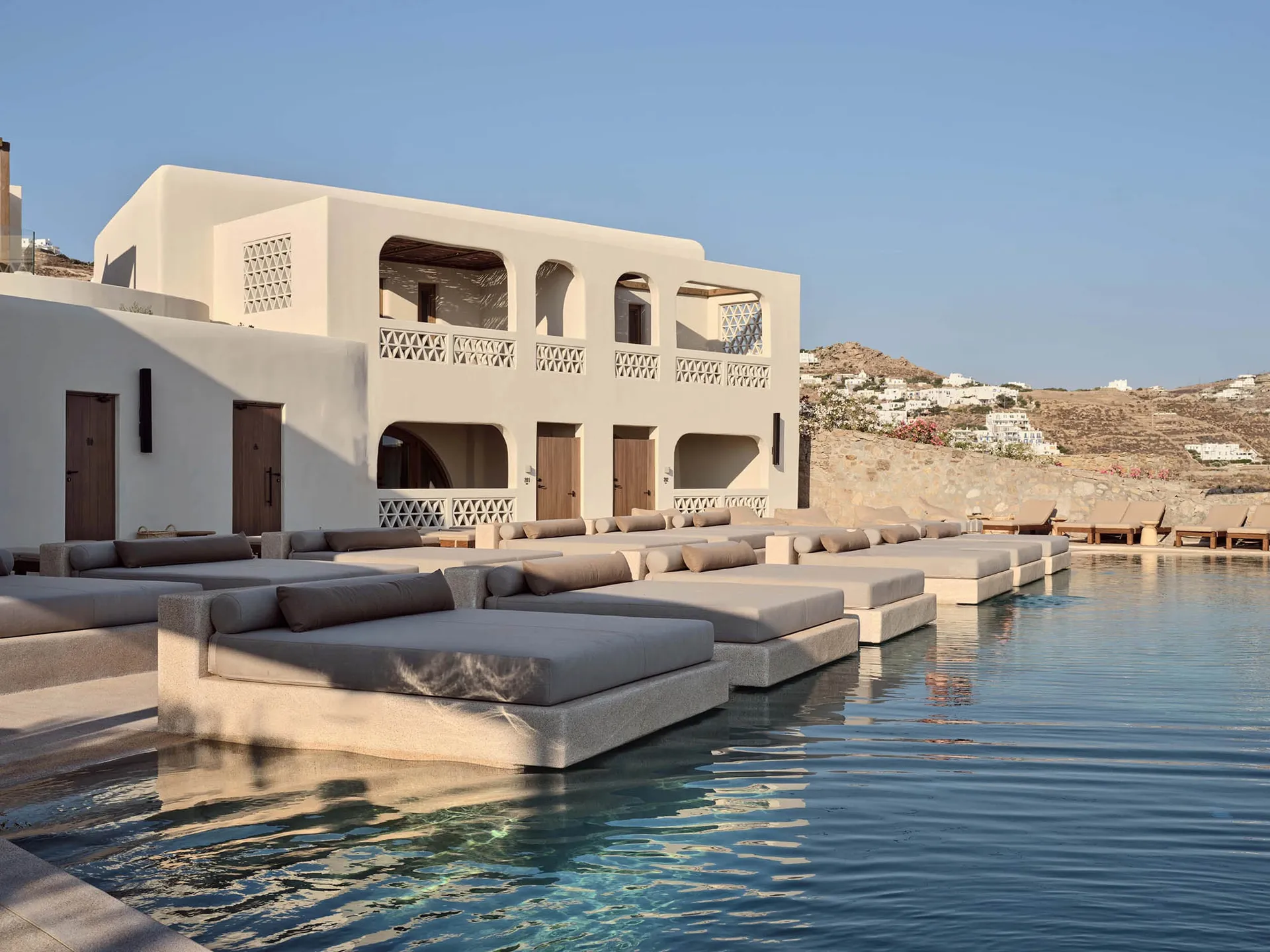 Modern poolside lounge setup with concrete benches and cushions surrounded by tranquil water.