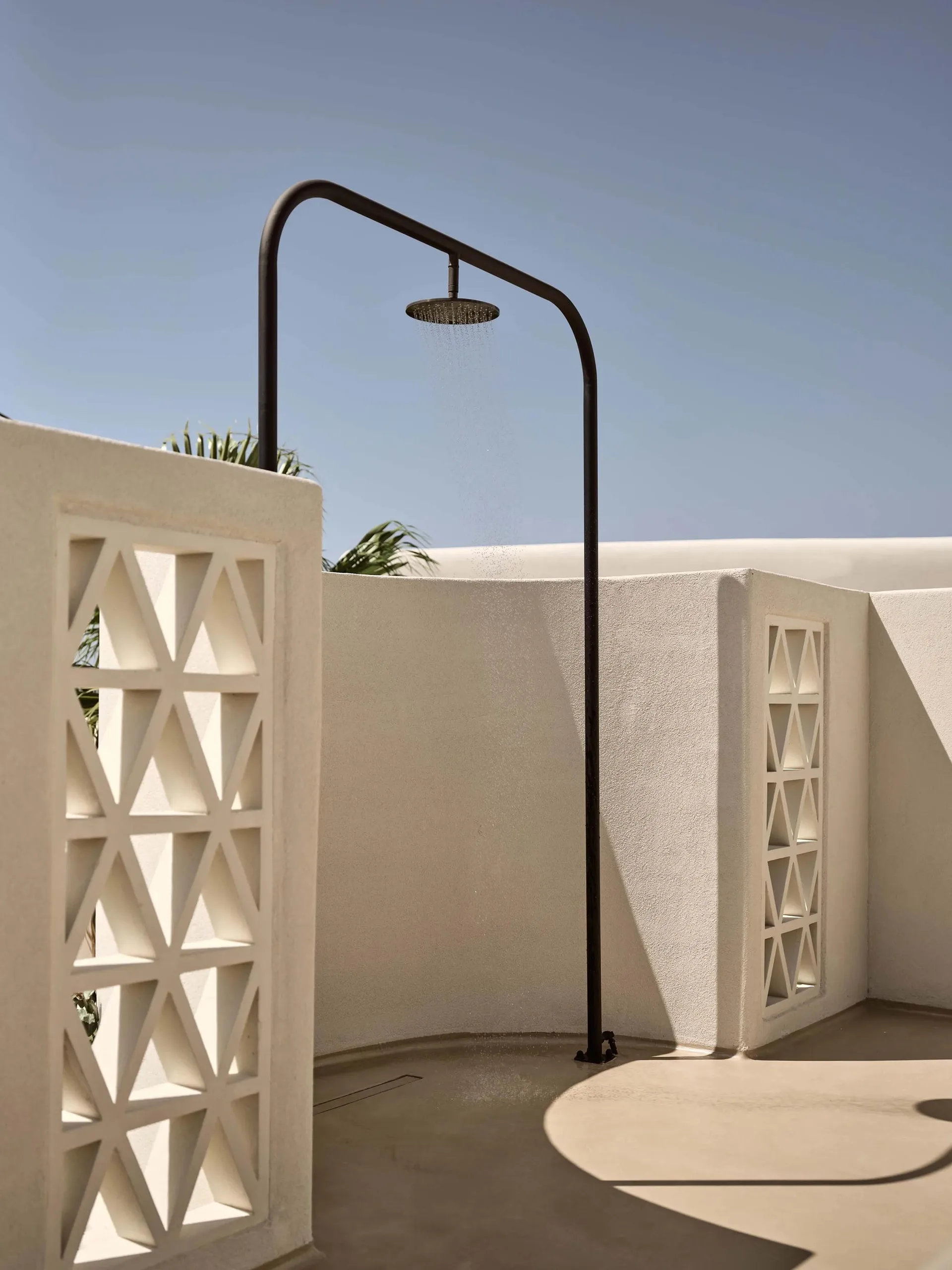 A minimalist outdoor shower with a metal frame, against a clear blue sky.