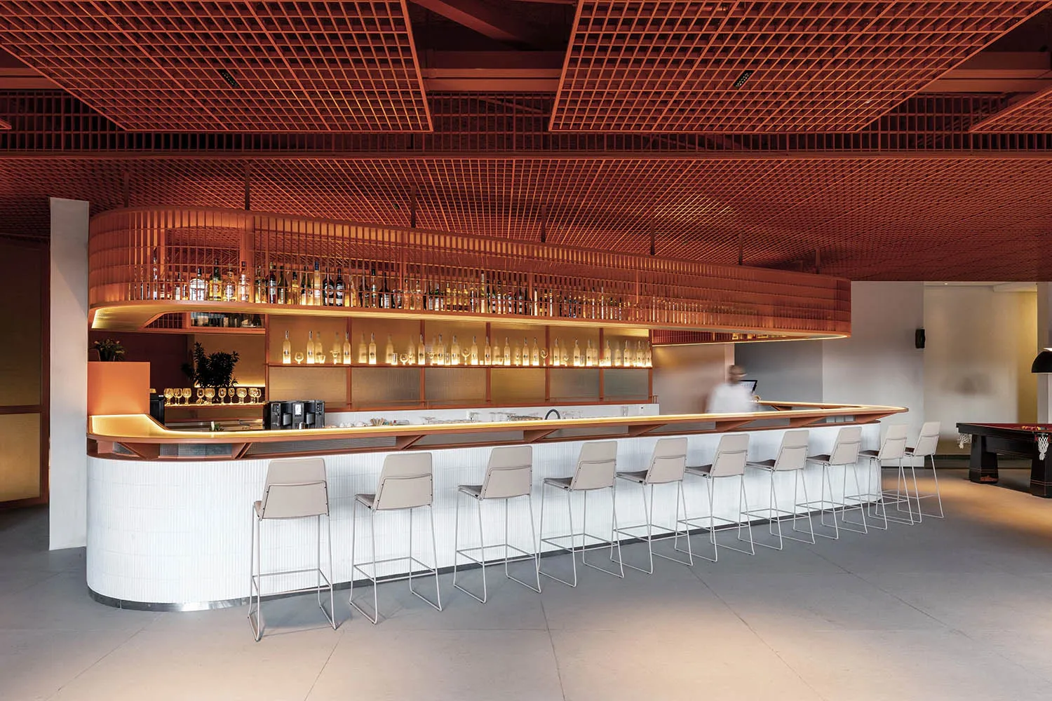 A modern bar with a wooden honeycomb grid ceiling and white stools.