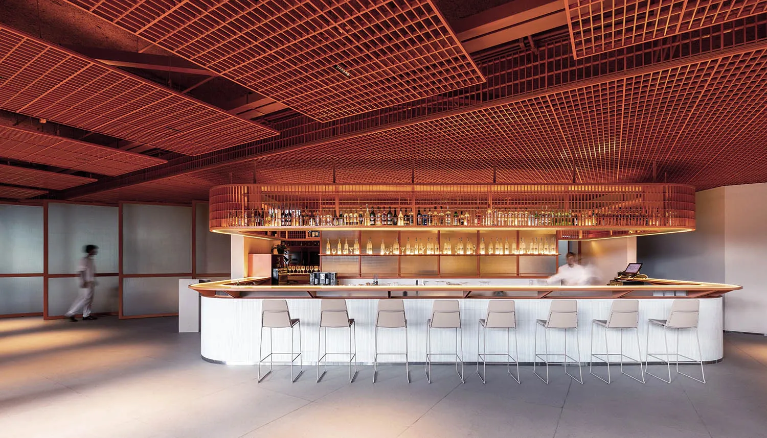 A minimalist bar counter with metal stools and a metal ceiling grid