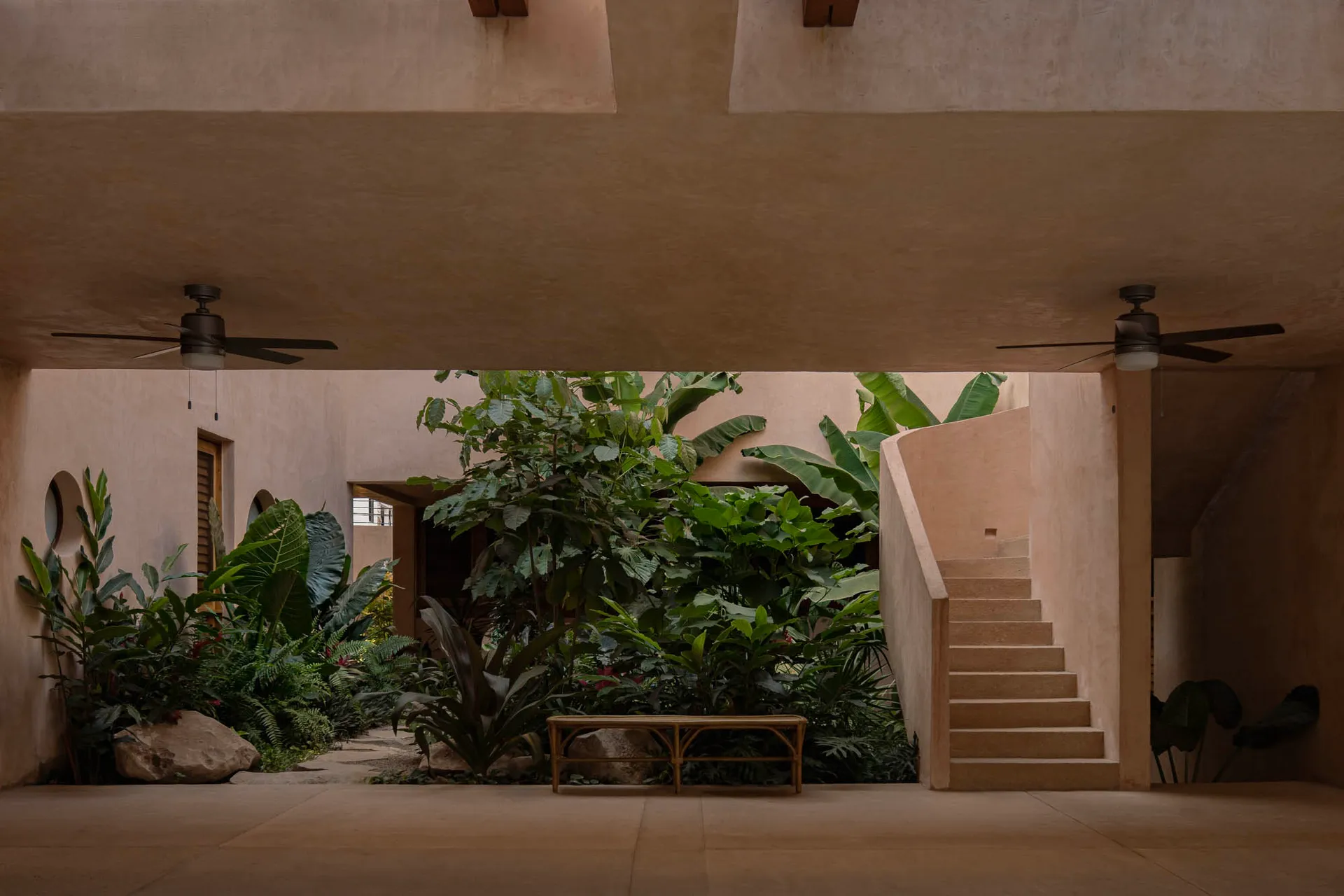 A modern interior space featuring concrete materials, with greenery and steps leading to a garden courtyard.
