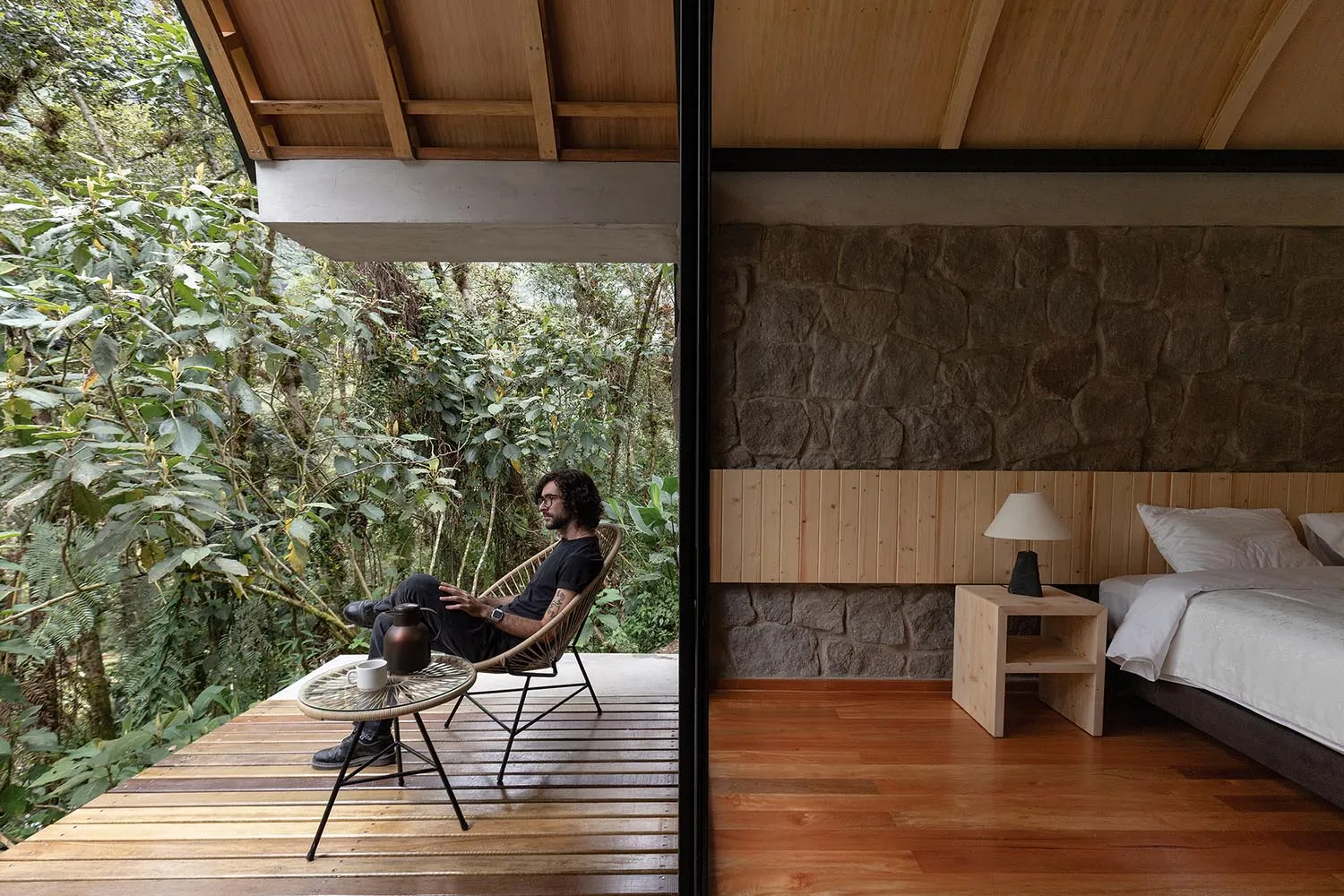 A modern minimalist bedroom featuring a wooden floor, stone wall, and simple furniture.