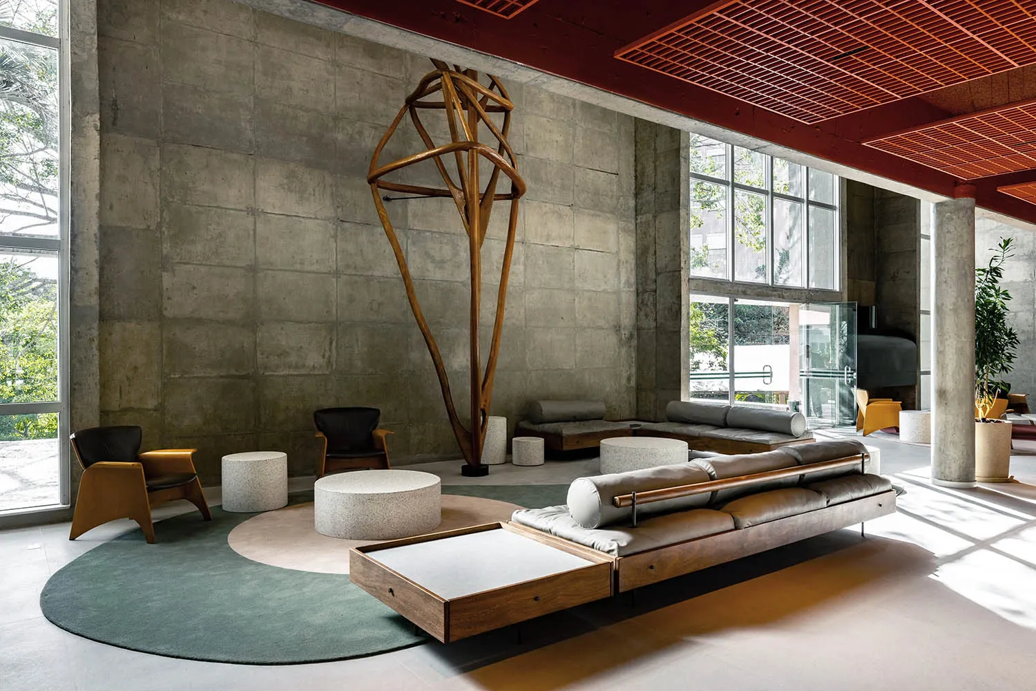 A minimalist lobby with concrete walls and floor, featuring modern furniture and a large geometric wooden sculpture.