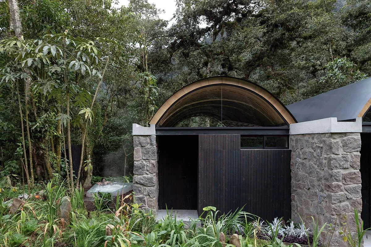 A modern minimalist spa hotel entrance featuring stone and wooden elements surrounded by lush greenery.