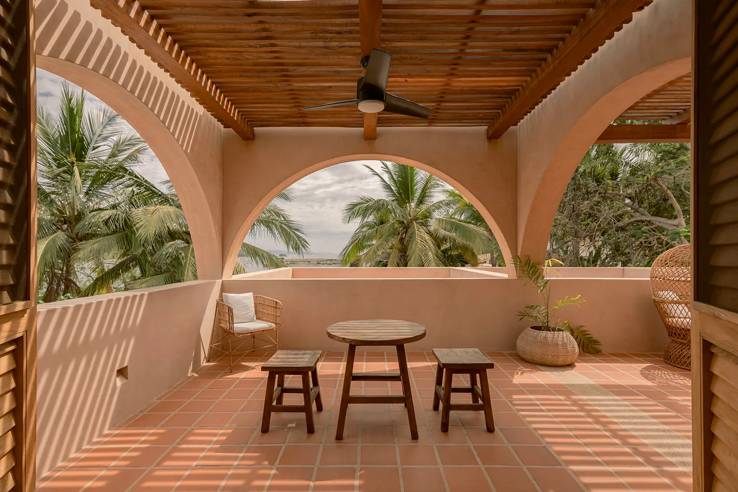 Vacation home veranda with wooden pergola, terracotta tiles, and tropical foliage.
