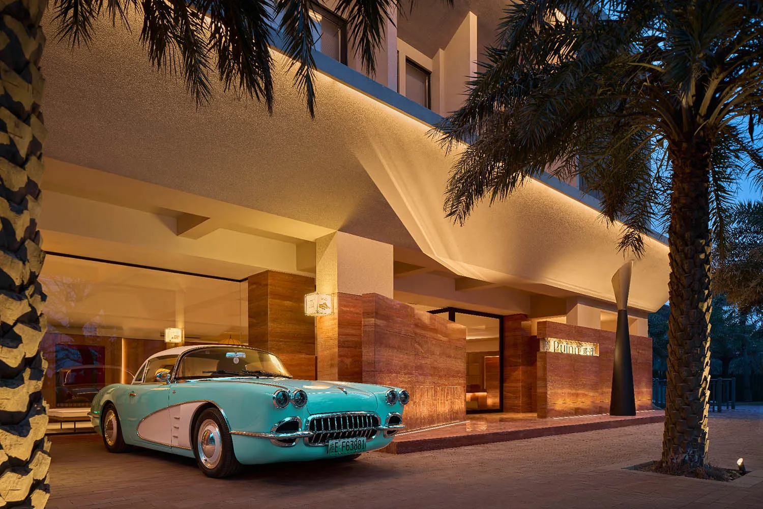 A classic blue and white car parked in front of a luxurious hotel entrance with concrete and marble finishes.