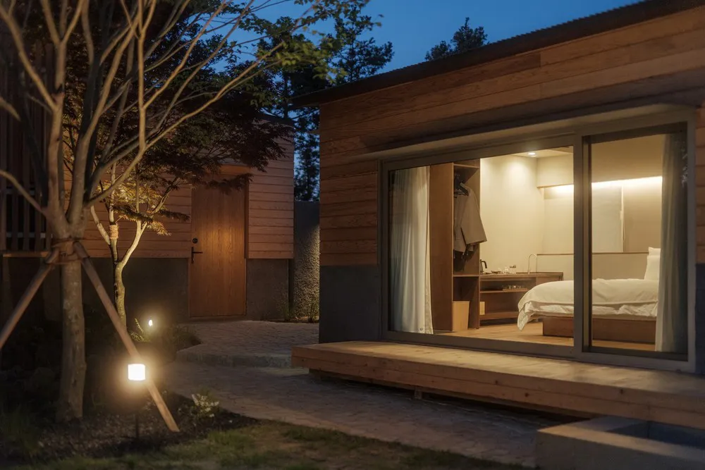 A serene, minimalist bedroom featuring wooden furnishings and a window overlooking the surrounding trees.