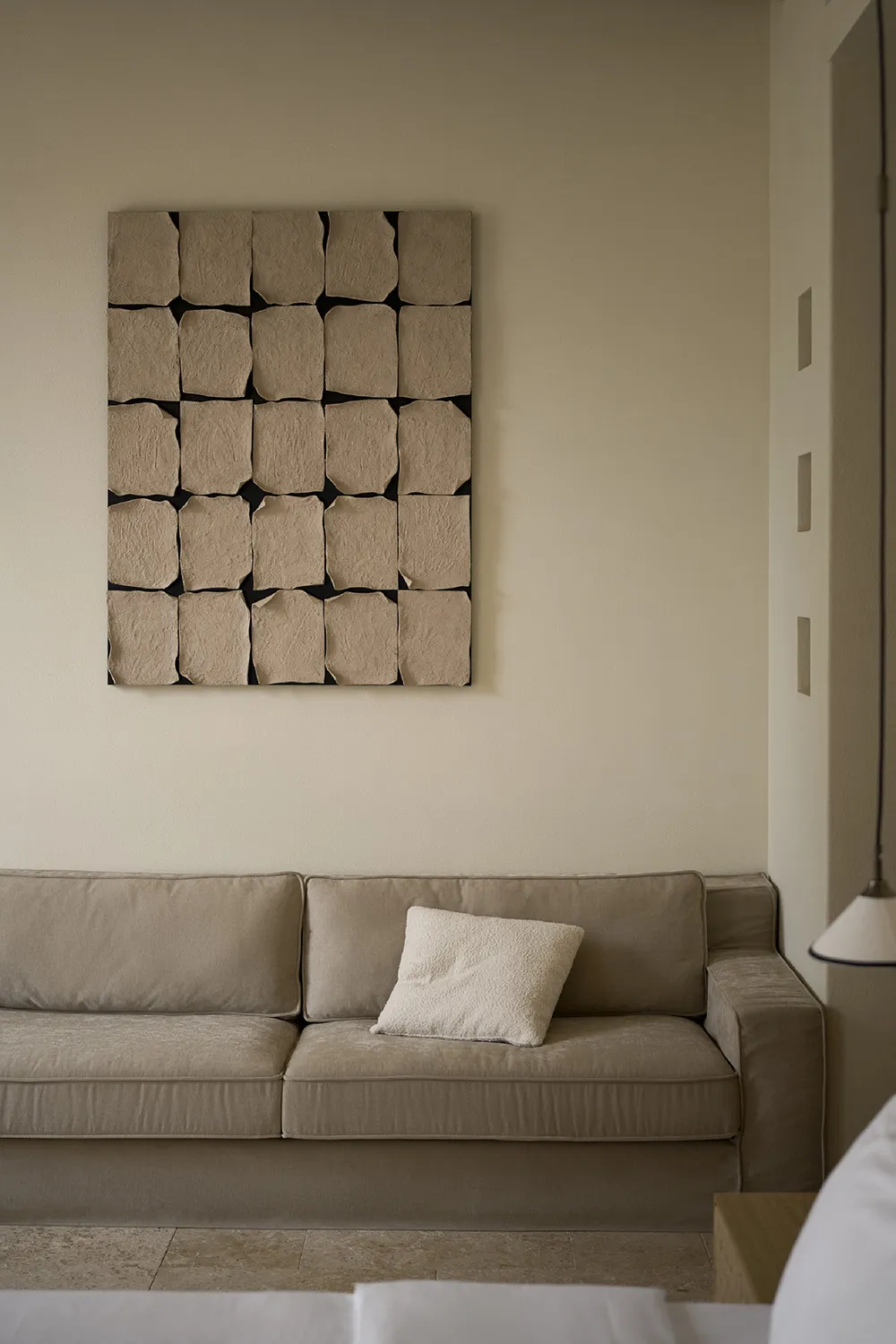 Modern, minimalist living room featuring a beige sofa with a textured fabric and a wall art piece composed of textured paper