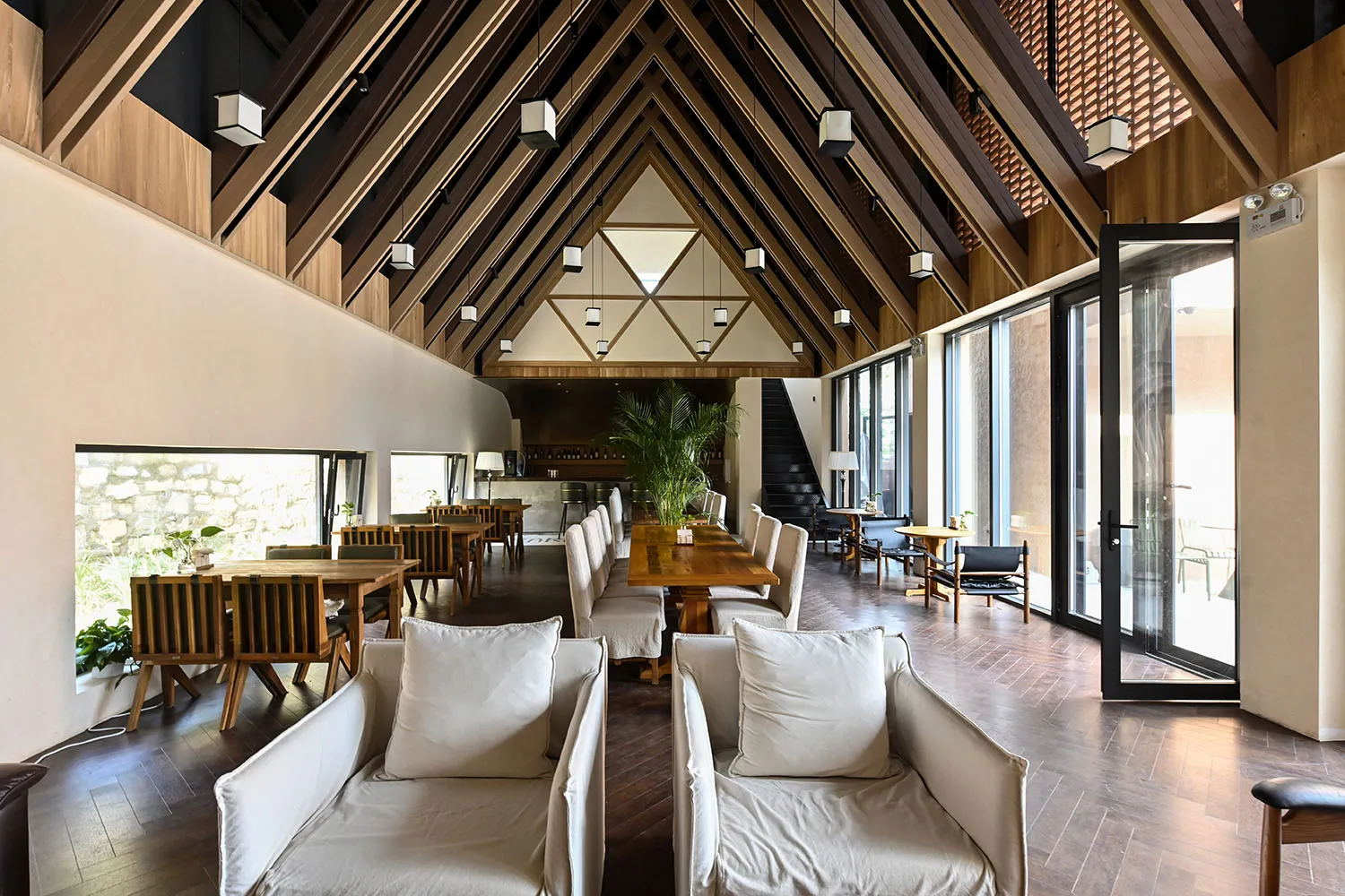 Modern restaurant interior with a high ceiling, wooden beams, and a mix of seating arrangements.