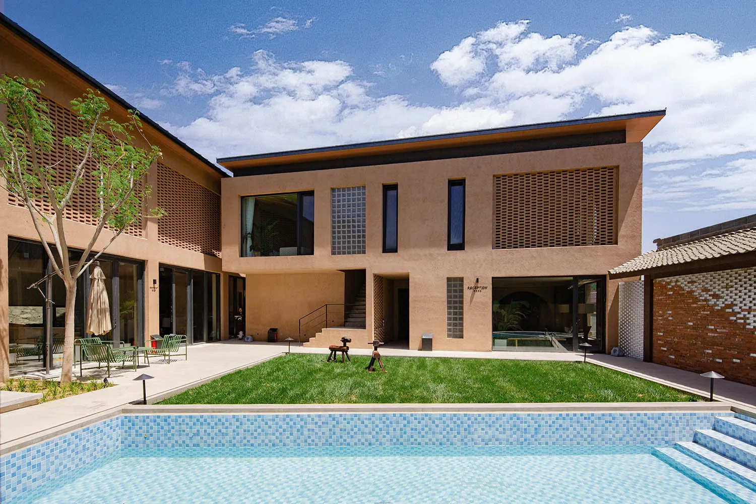 A two-story modern house with a concrete exterior and a pool in the foreground.