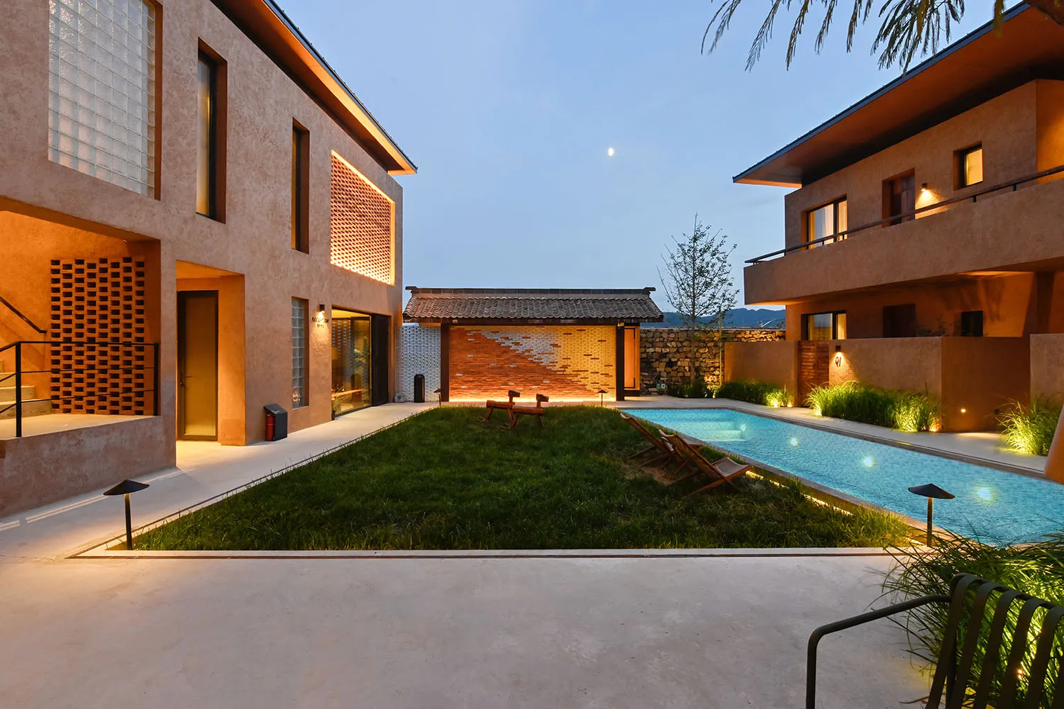 A modern residential building with a concrete exterior and a courtyard with a pool and greenery at dusk.