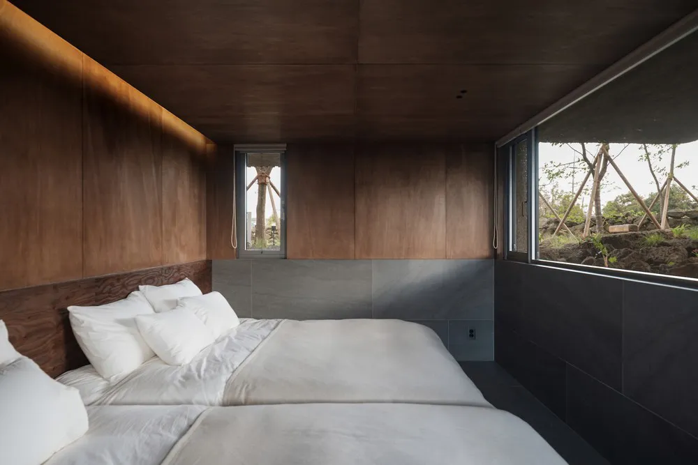 A minimalist bedroom featuring a bed with white bedding and wooden walls, viewed from the side.