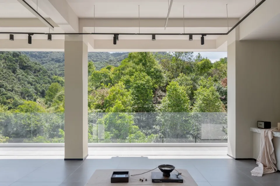 A modern living room with a large glass window overlooking lush greenery and mountains.