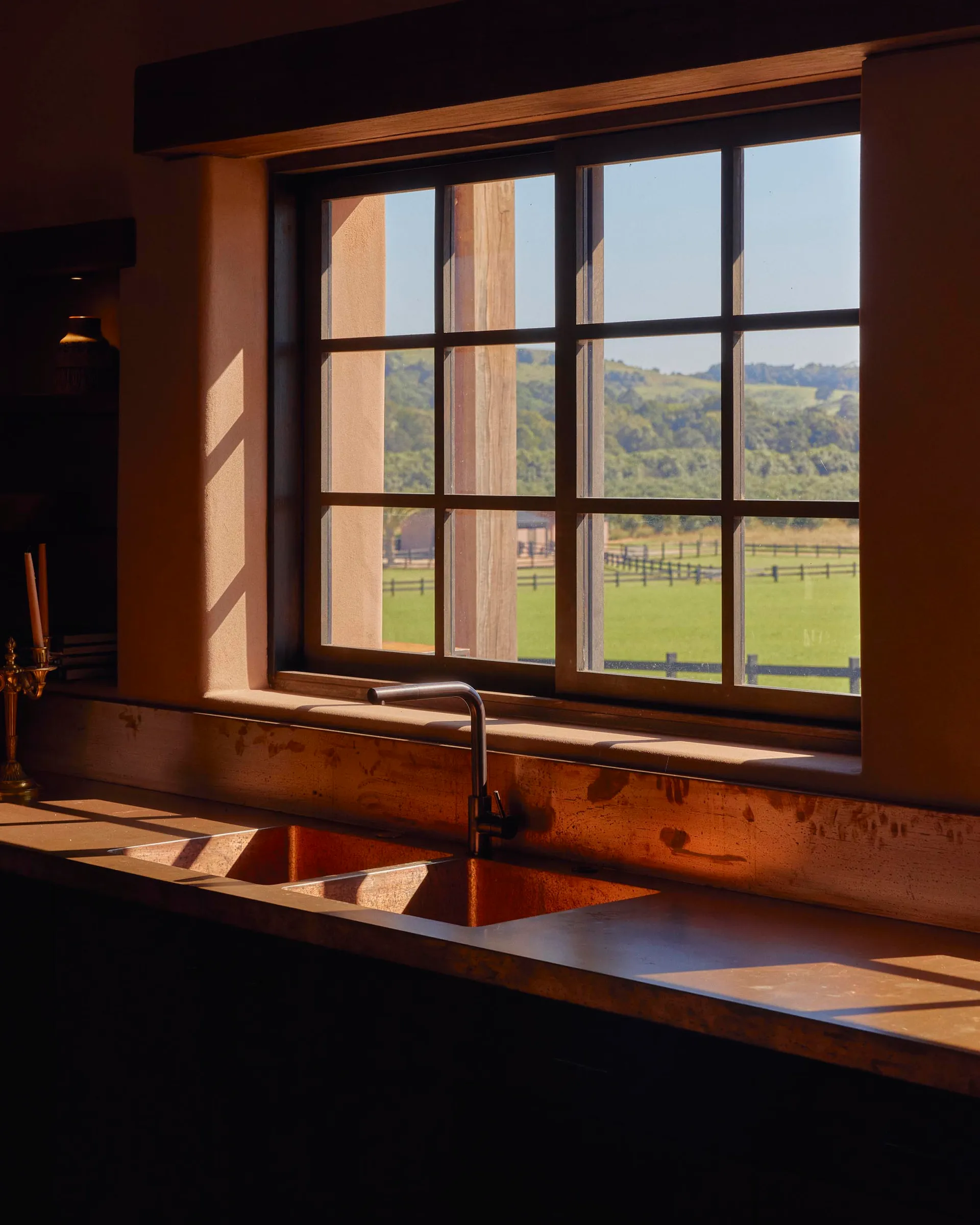 Modern kitchen scene featuring a copper sink with backlit countertop, overlooking a lush green landscape with a wooden frame