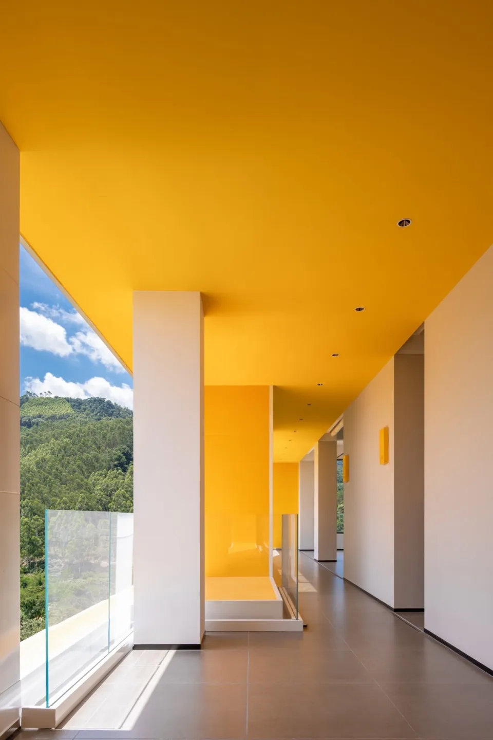 A modern interior with large windows, concrete walls, and yellow-painted ceiling and floor.