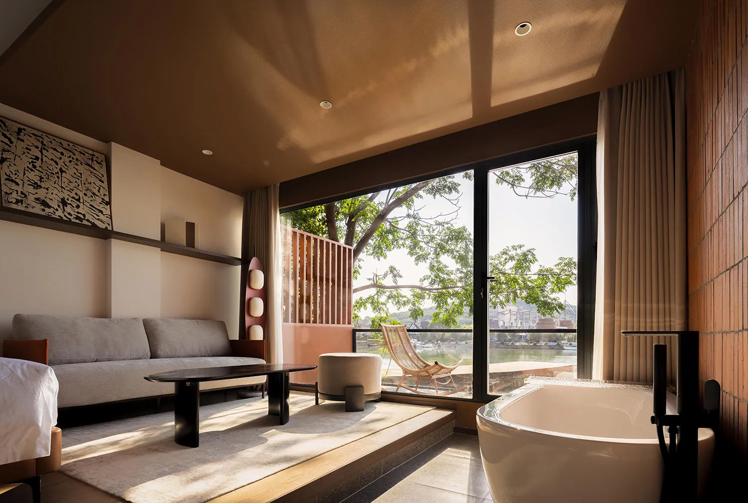 A minimalist hotel suite featuring concrete walls, wooden furniture, and floor-to-ceiling windows with a view of the outdoors