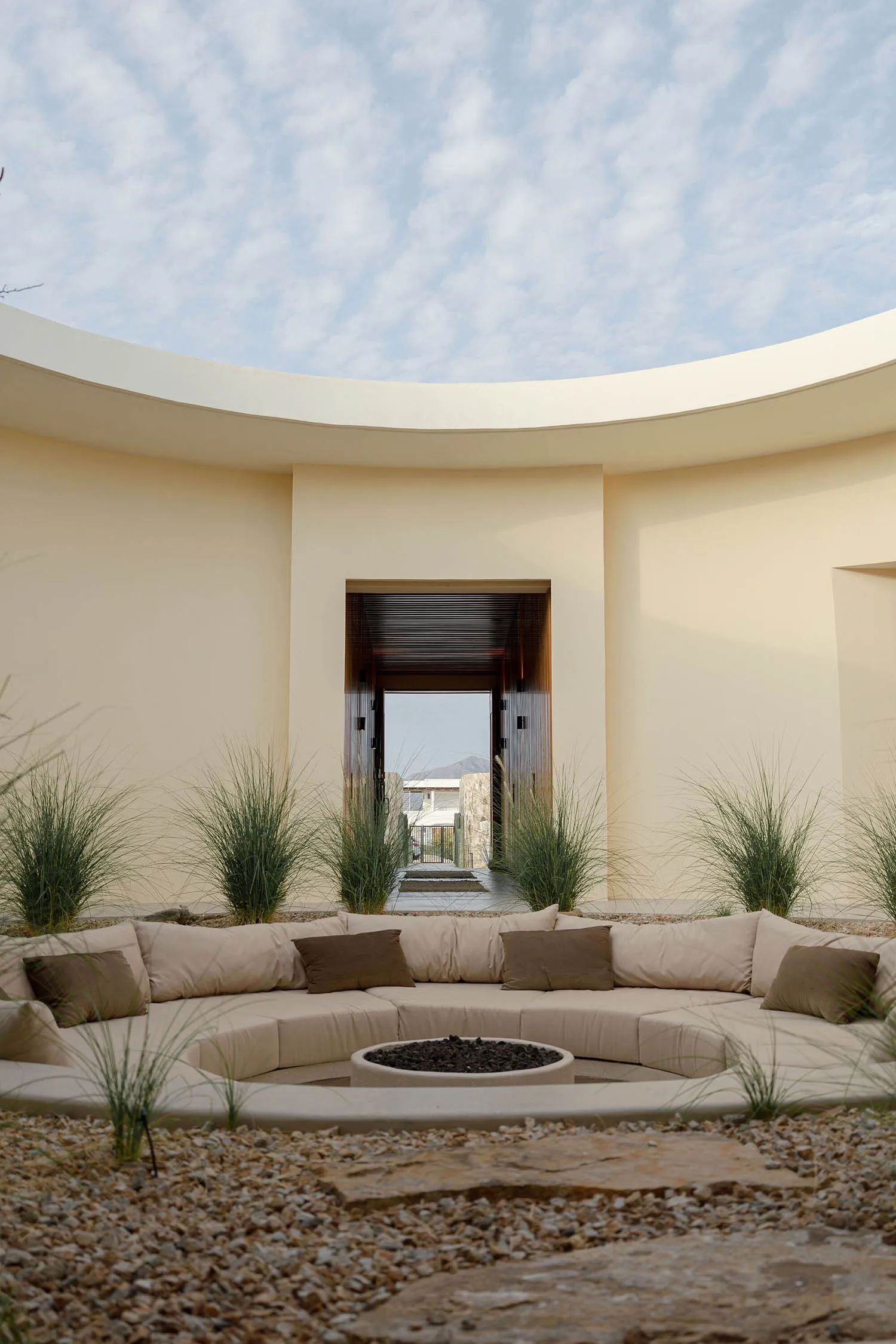 A modern architectural exterior featuring a circular, concrete space with seating and a fire pit.