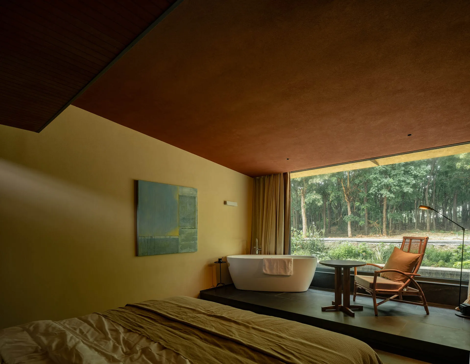 Modern bedroom featuring a ceramic armchair, a large window with a view of a forest, and a freestanding bathtub.