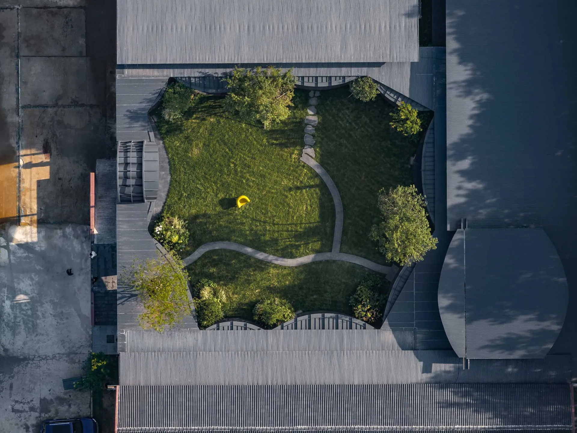 現代風格的綠意花園，設有黃色雕塑與彎曲步道，四周被建築環繞。