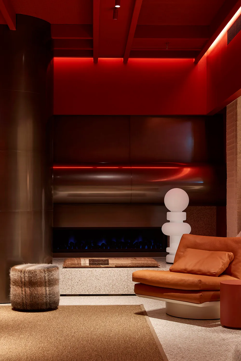 A modern living room with concrete walls, a leather sofa, and a fireplace with red lighting.
