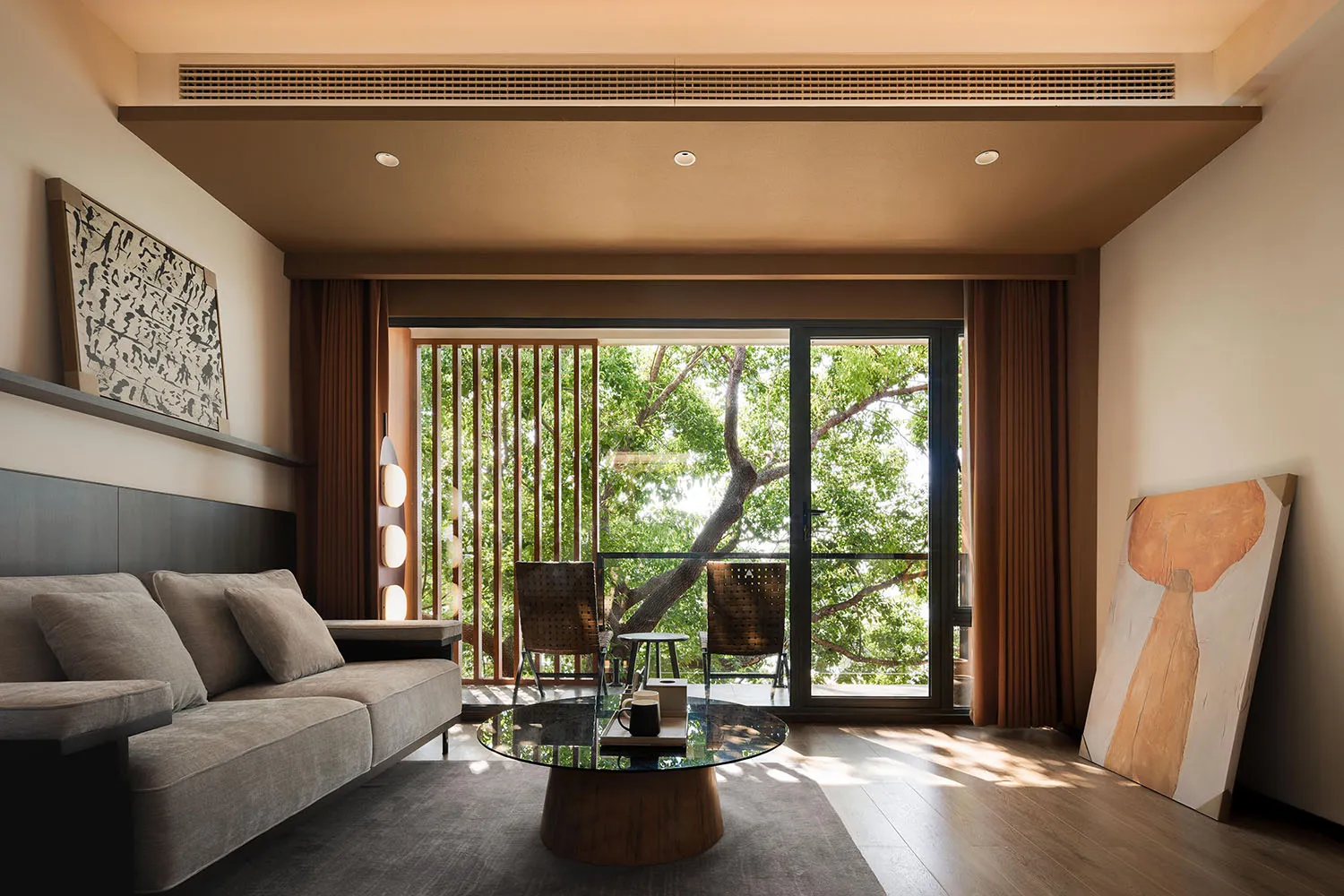 Modern minimalist living room with a warm color palette, featuring a grey sofa, a glass coffee table, and large windows overl