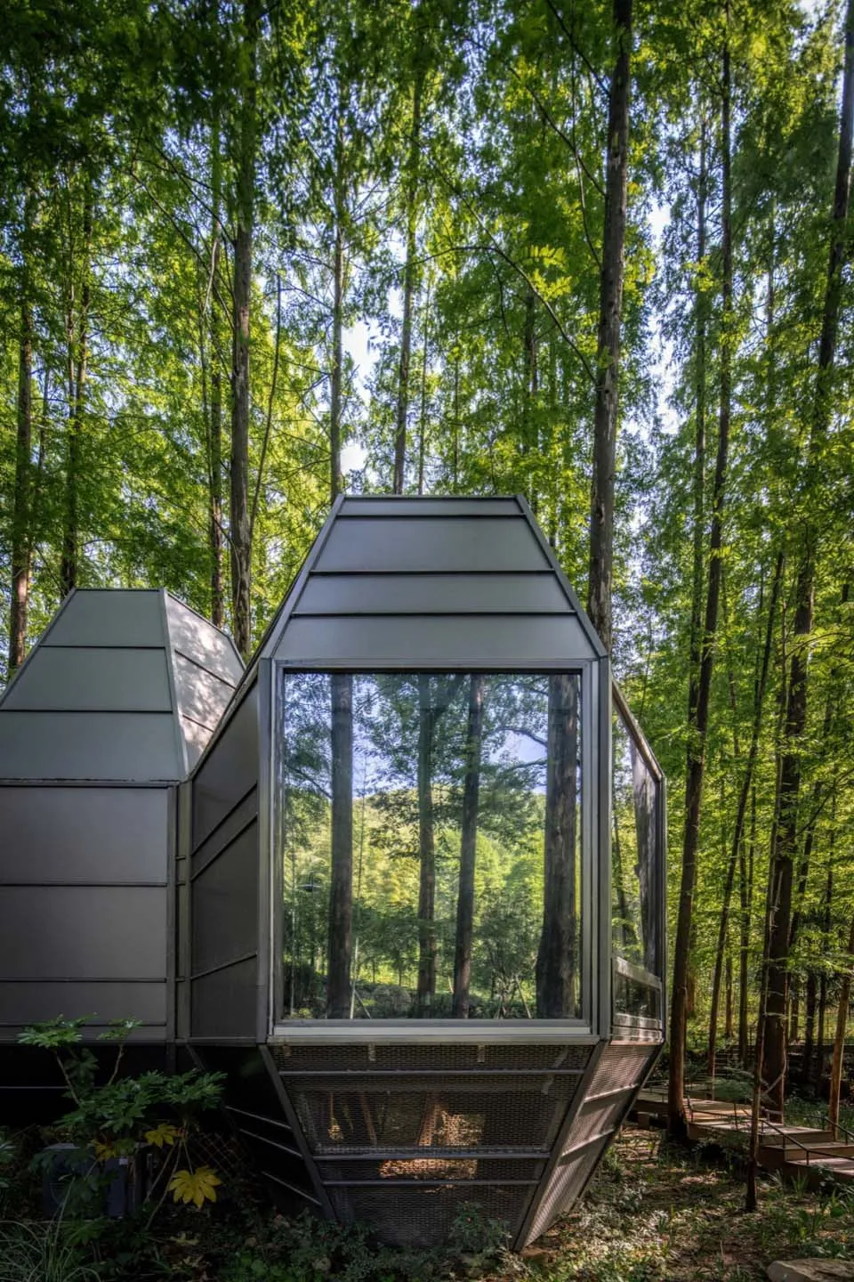 A modern modular house with metallic and glass elements in a forested setting.