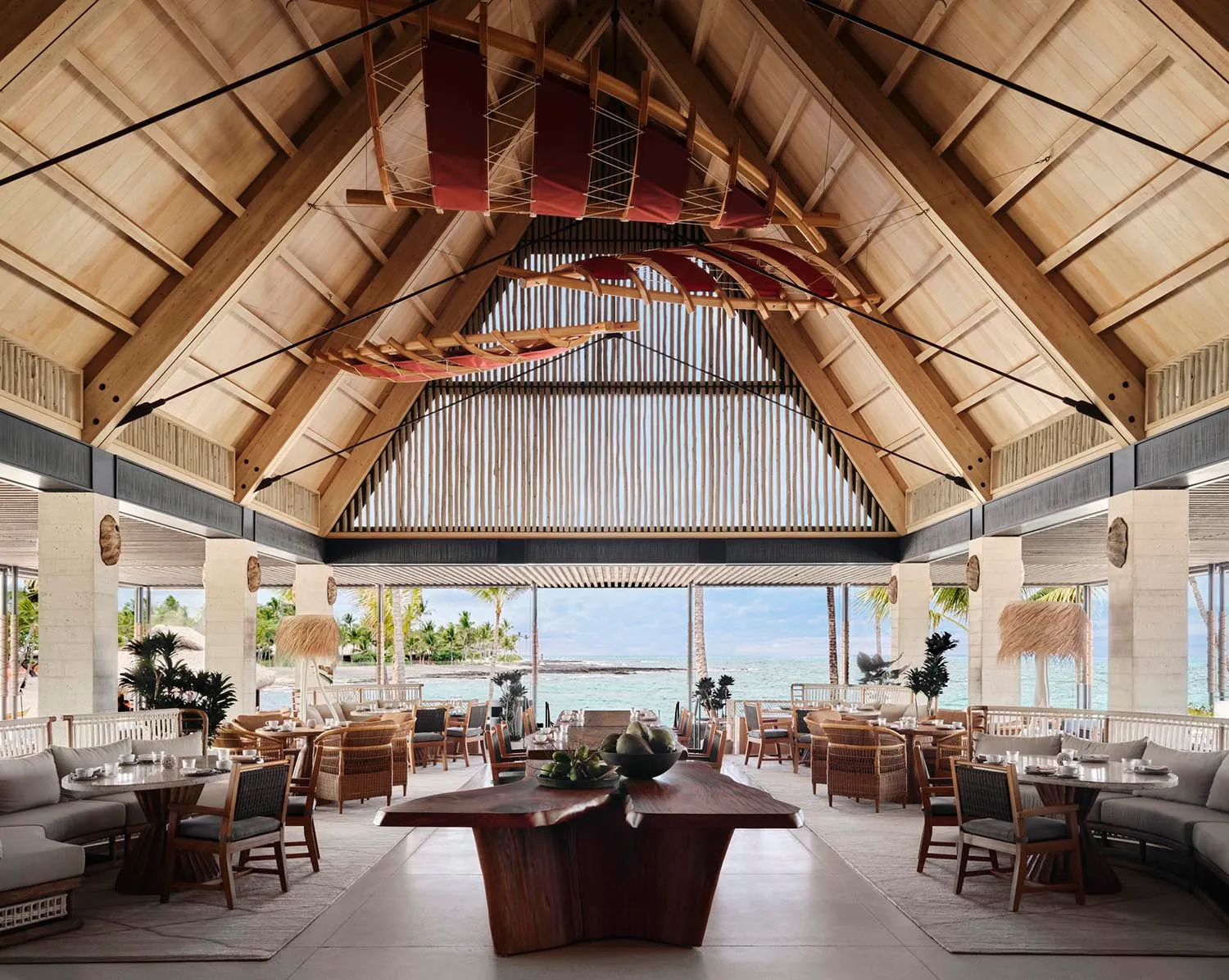 A spacious restaurant interior featuring wooden beams, open layout, and a view of the ocean.