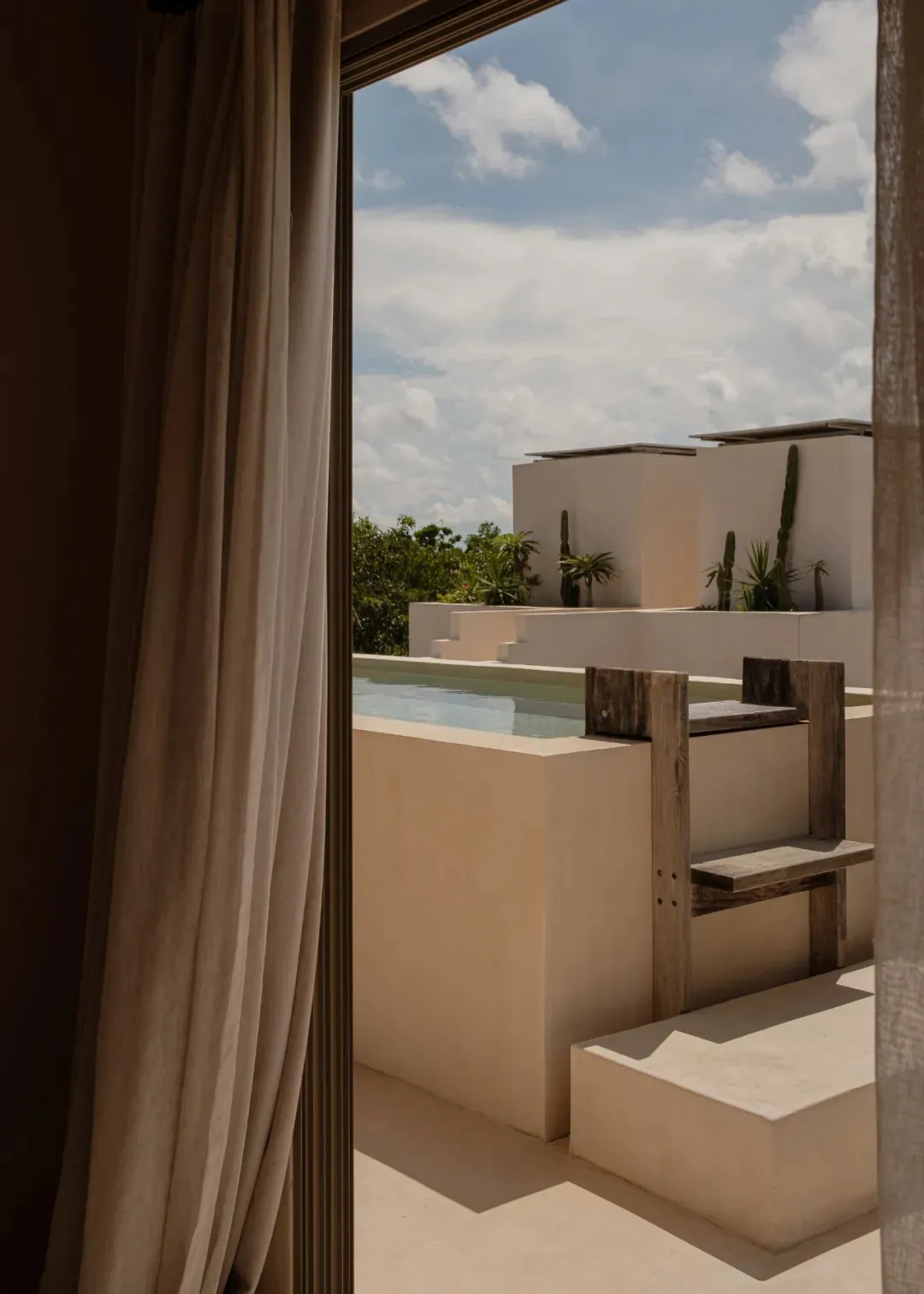 A minimalist patio area with a concrete surface and a wooden pool ladder, featuring an ocean view.