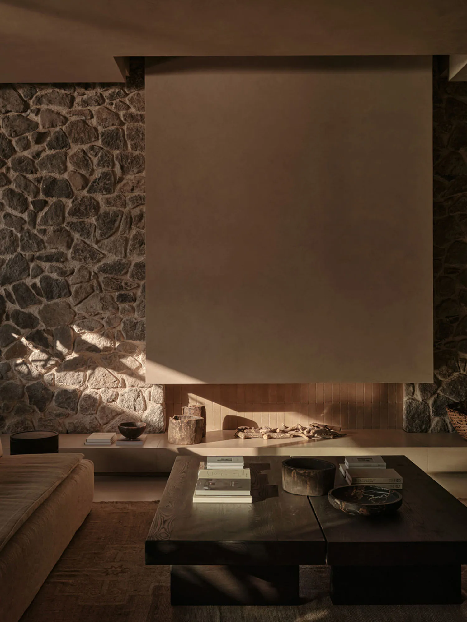 A modern living room with warm, earthy tones featuring a low wooden coffee table and a cozy stone fireplace.