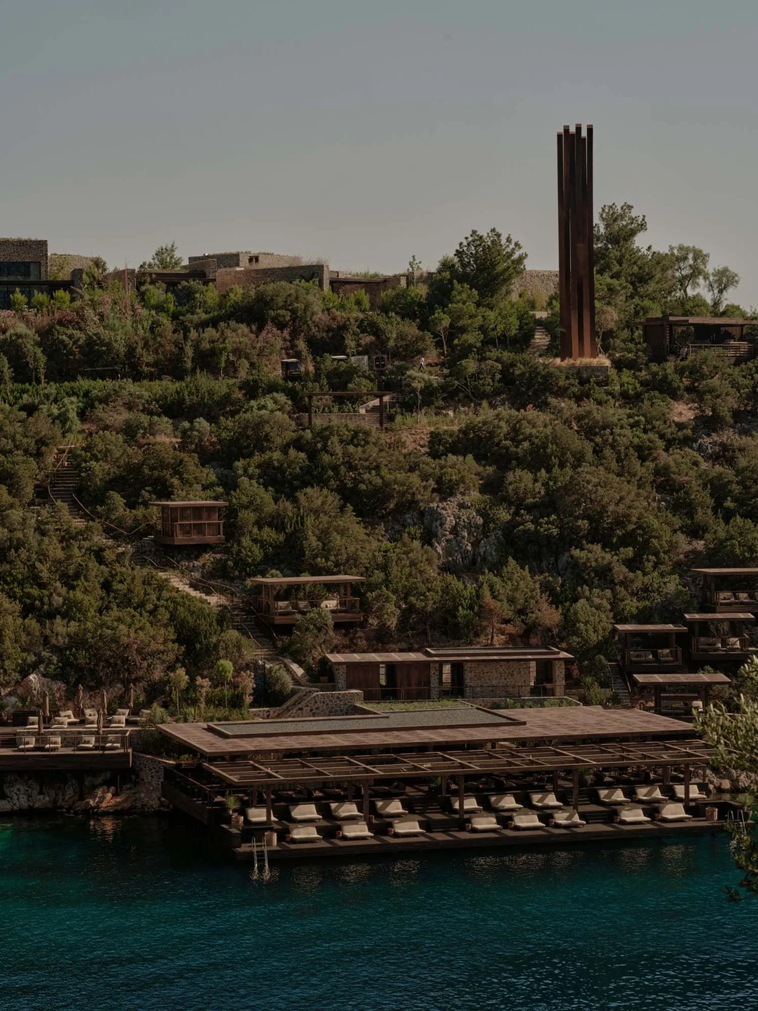 A resort with wooden structures, stone terraces, metal columns, and glass walls and windows.
