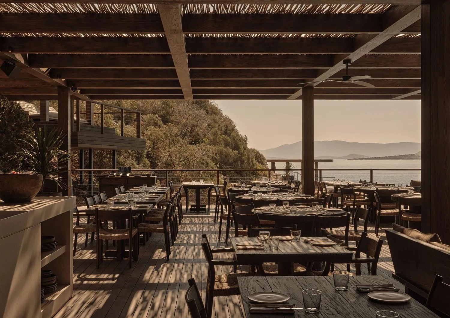 Well-dressed tables in a wooden restaurant setting overlooking the ocean.
