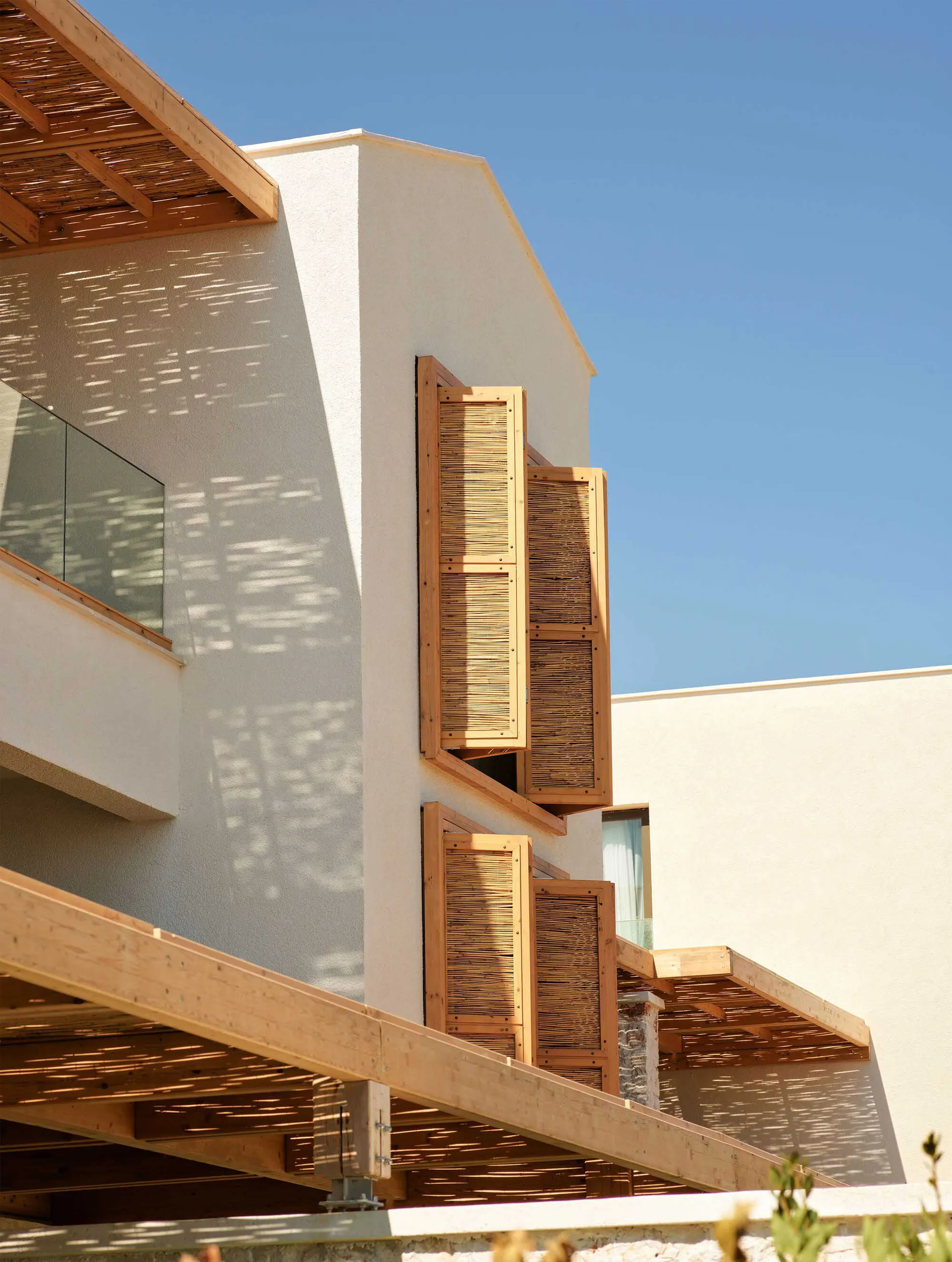 Modern building exterior featuring wooden shutters and balconies with sunlit shadows.