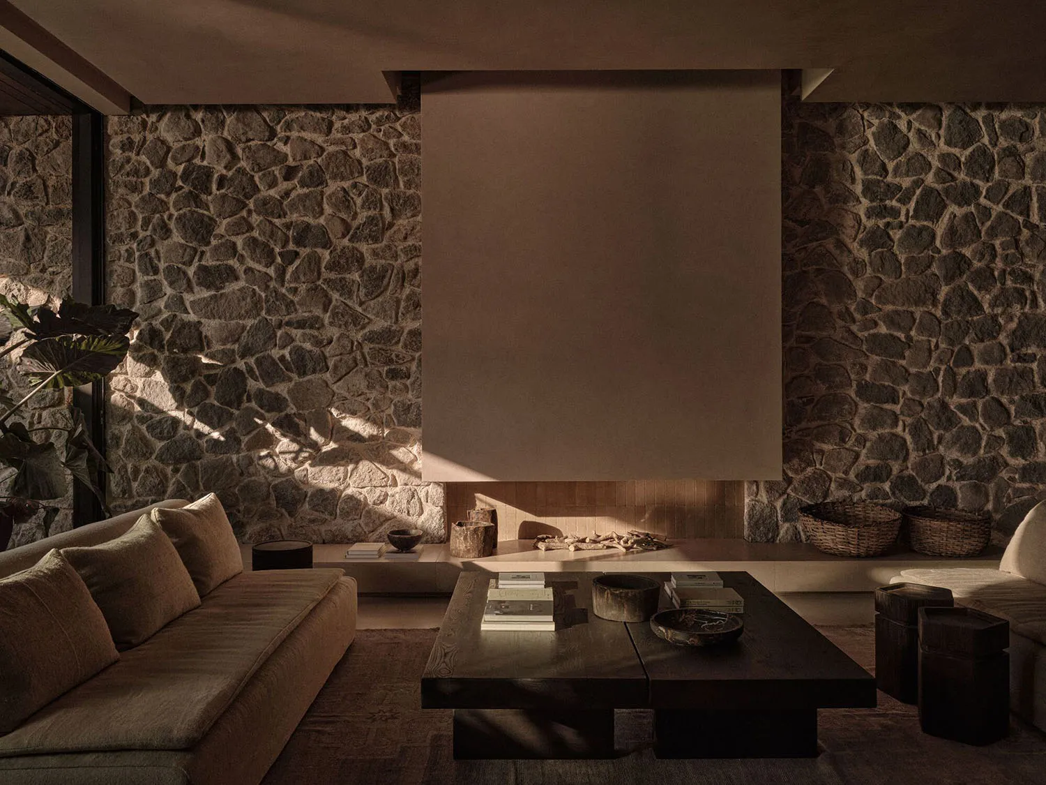 A modern living room with a stone wall, a wooden coffee table, and a large screen.