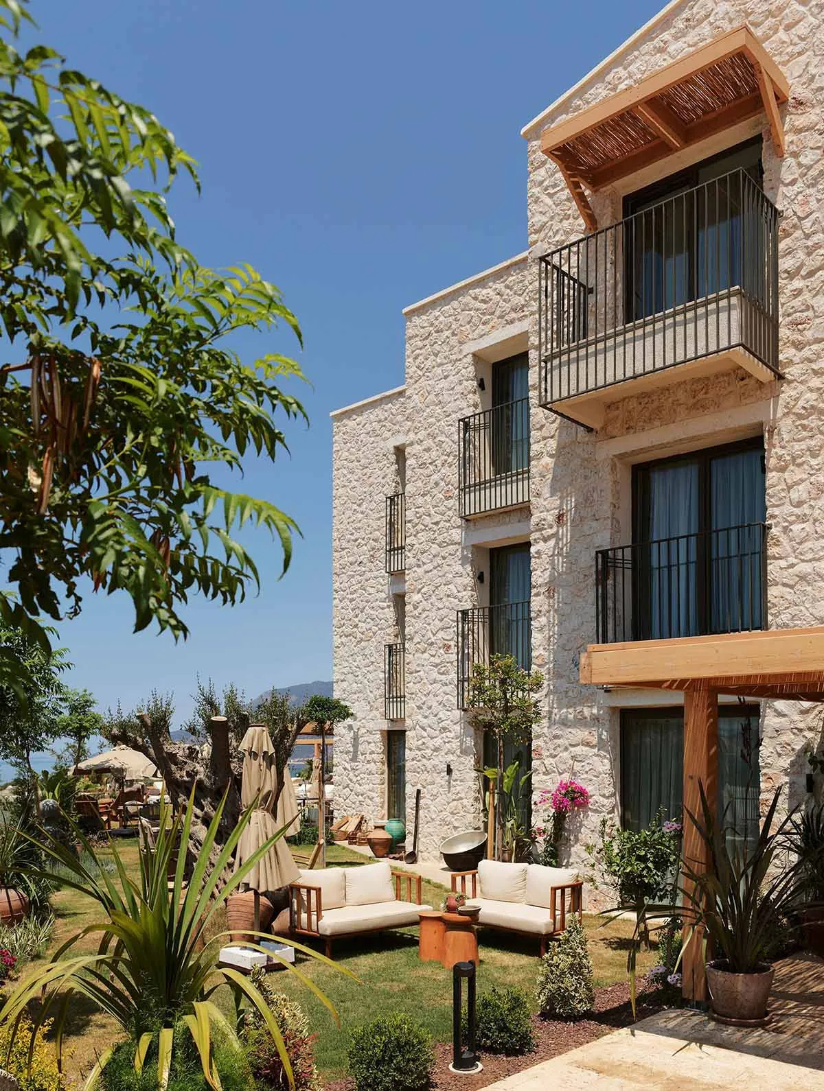 A modern residential house with stone exterior and garden area with patio furniture and greenery.