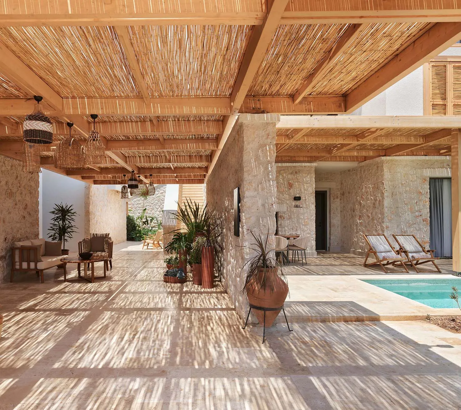 A wooden patio with a pergola structure, plants, and lounge furniture under a clear sky.