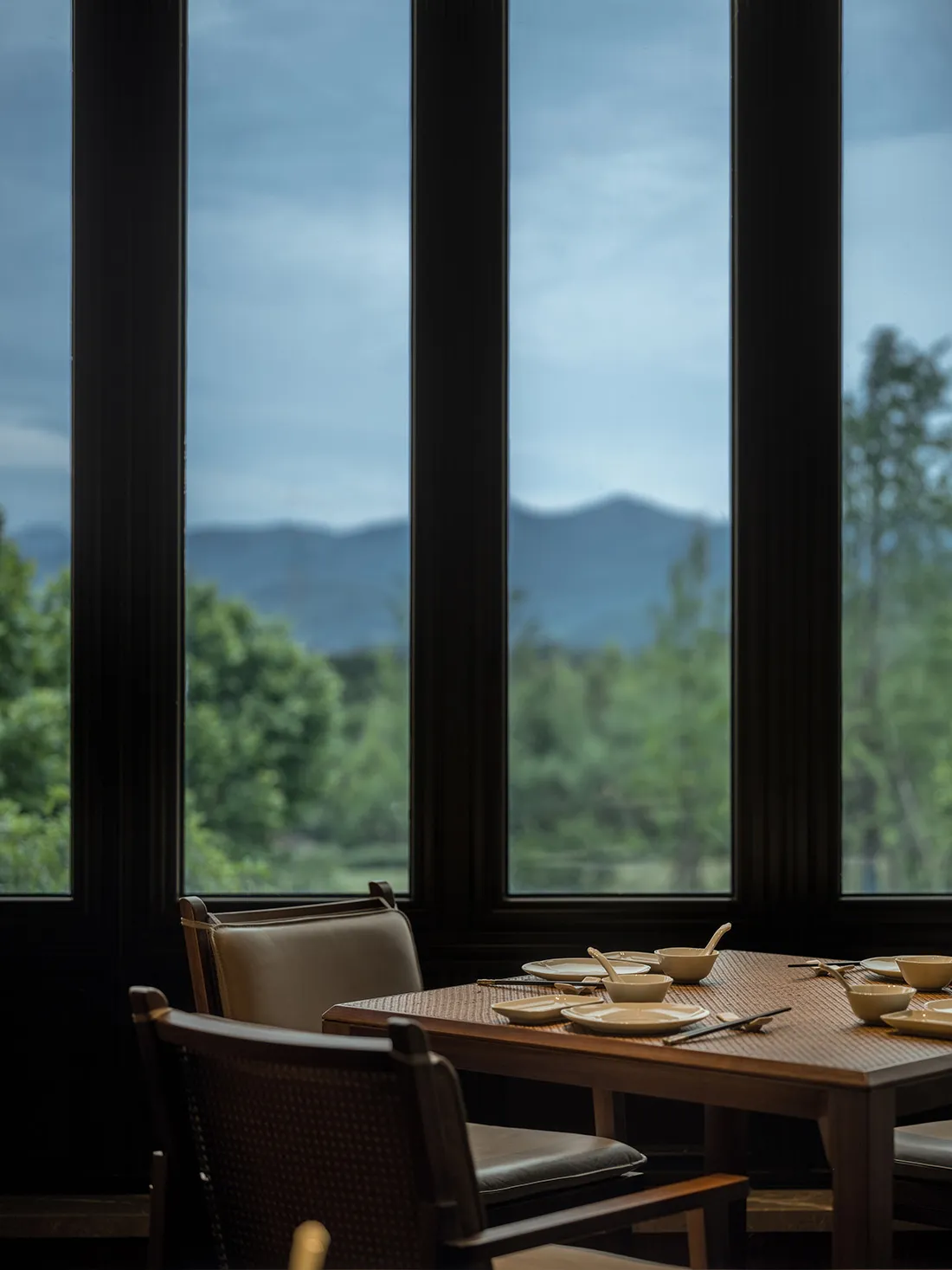 A modern restaurant interior featuring glass walls and wooden dining tables.