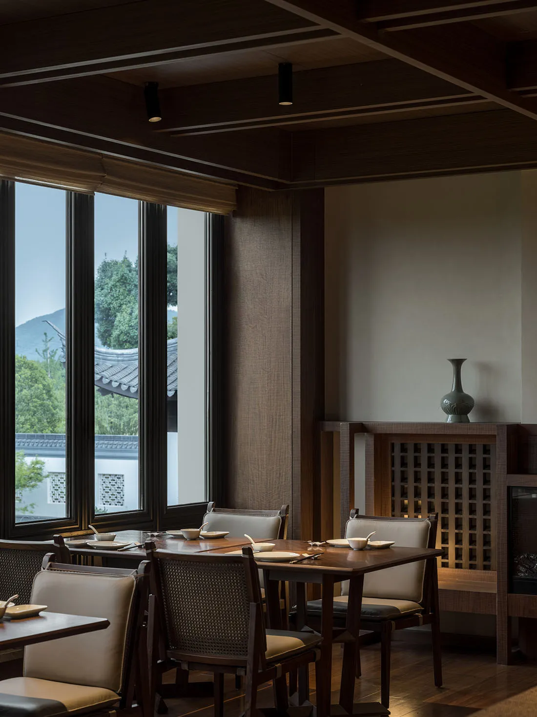 A modern restaurant interior featuring wooden tables and chairs, with large windows showcasing a scenic view of mountains and