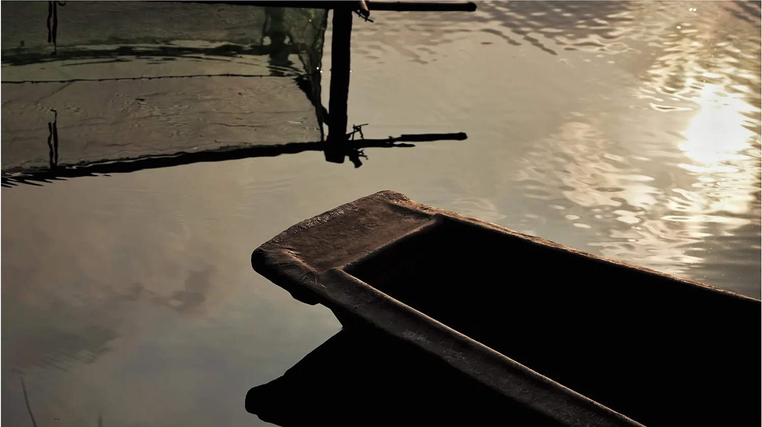 A wooden boat floating on calm waters with a reflection of a wooden post and rope in the background.