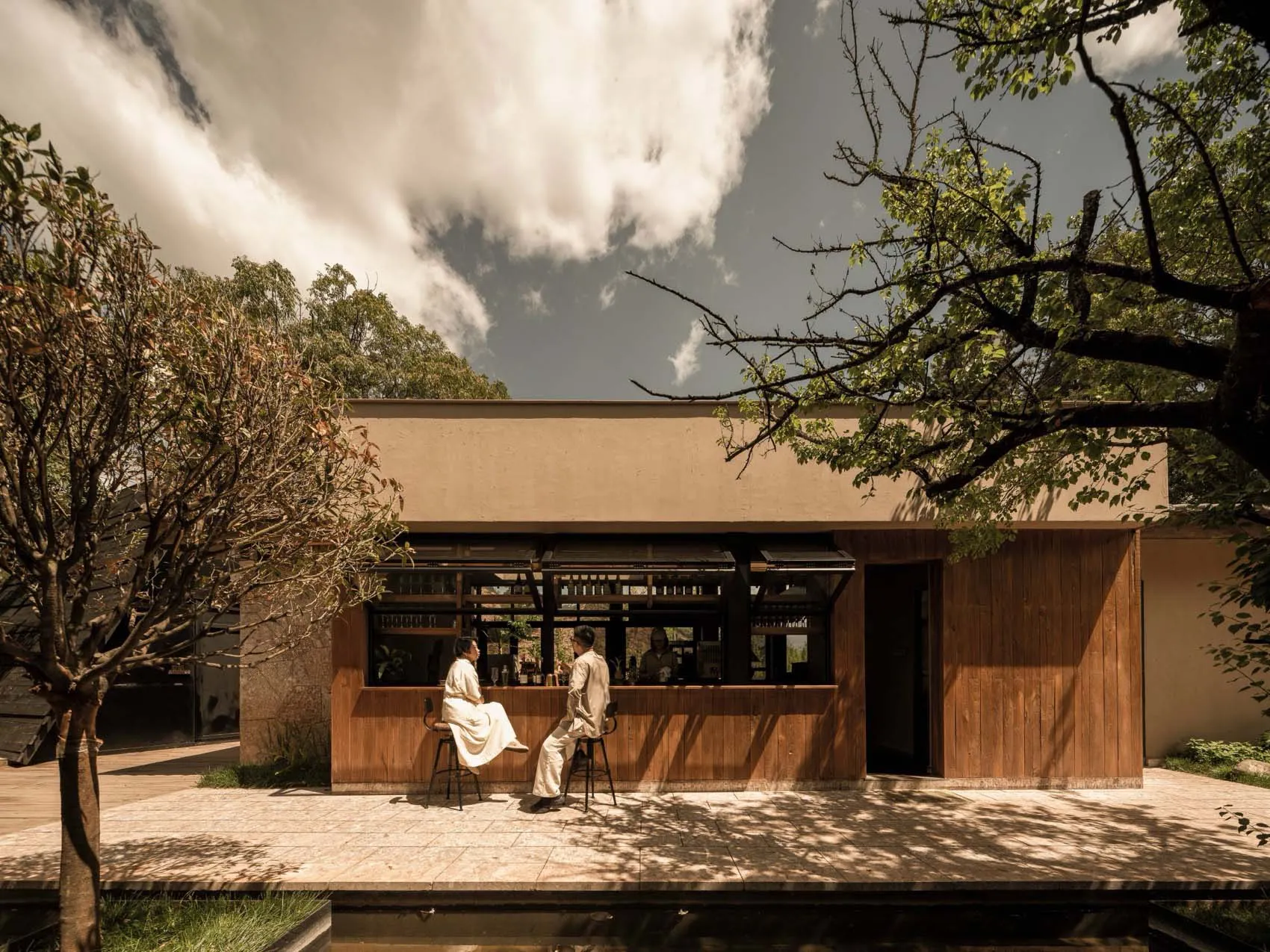 People enjoying drinks at a minimalist cafe with wooden features and outdoor seating.