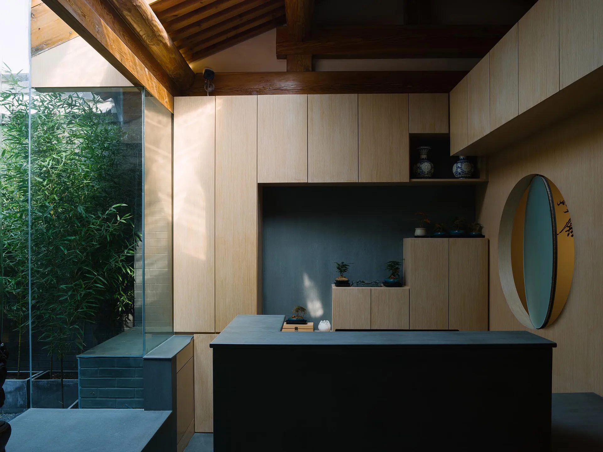 A minimalist office space featuring wooden walls and cabinets, with a large window and greenery visible.